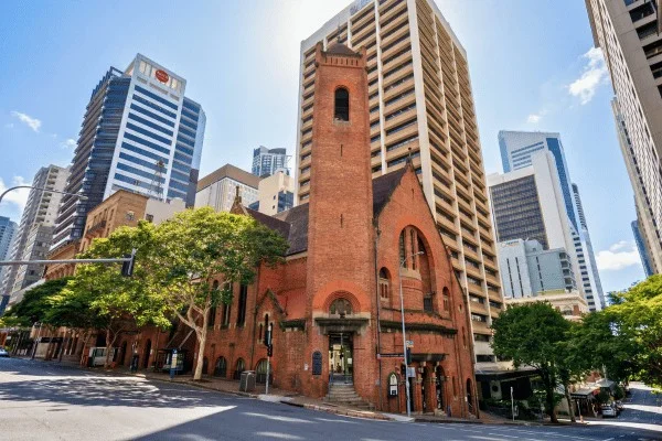Eine ältere Backsteinkirche steht zwischen modernen Hochhäusern und zeigt, wie sich die Dimensionen der Stadt verändert haben, die aus der Flusssiedlung entstand.