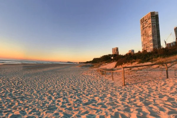 Una torre recibe el sol bajo sobre un tramo de playa y dunas.